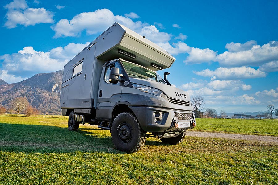 Artgerecht Iveco 4x4: Hellgraues Iveco-4x4-Fahrgestell mit Alkoven-Wohnkabine auf einer Wiese