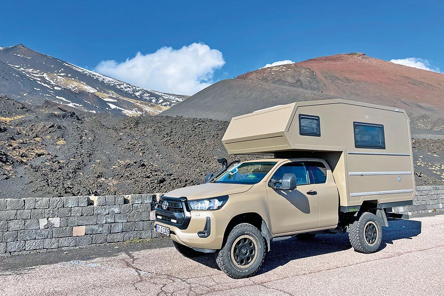 Beigefarbener Pick-up mit Alkoven-Wohnkabine in karger Berglandschaft