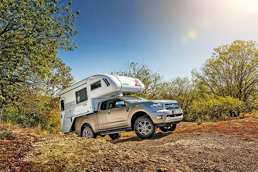 Grauer Pick-up mit weißer Alkoven-Wohnkabine offroad bergauf unterwegs