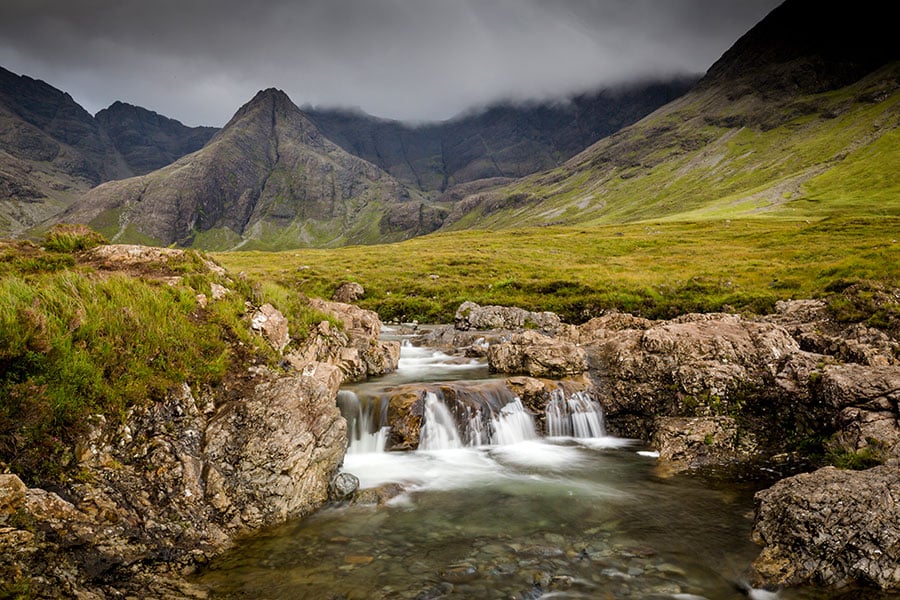 Bach und kleiner Wasserfall inmitten grüner Hügellandschaften
