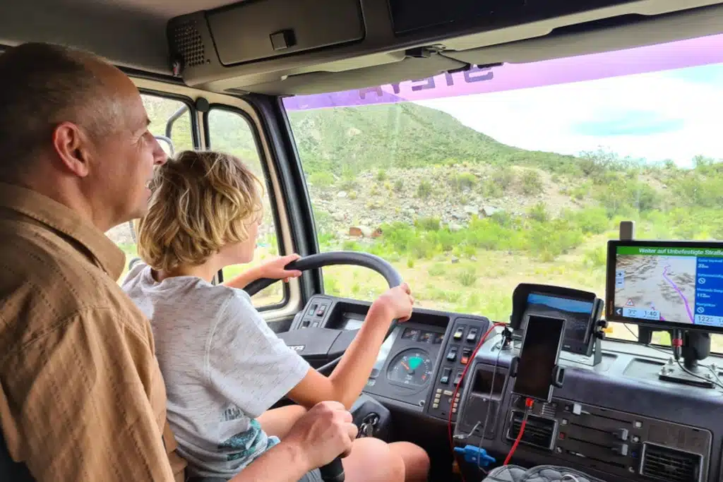 Junge auf Schoß von Vater am Steuer von Expeditionsfahrzeug