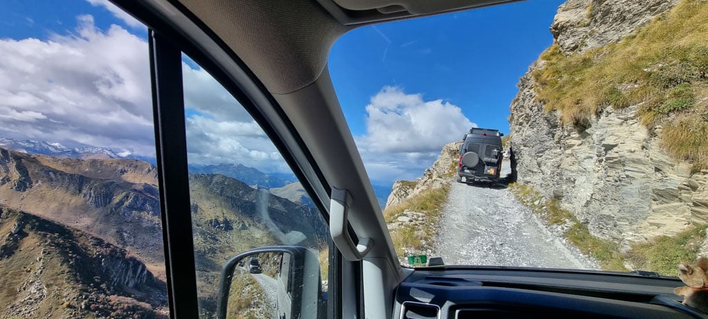 Blick aus einer Windschutzscheibe auf ein vorausfahrendes Fahrzeug auf einer schmalen Bergstraße