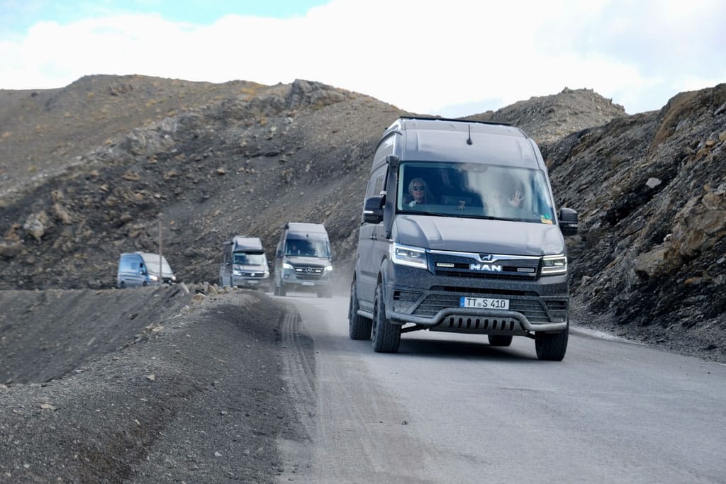 Vier Campervans fahren auf einer Straße entlang kargen Hügeln