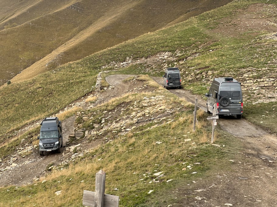 Drei Campingfahrzeuge auf einer schmalen Straße am Berghang