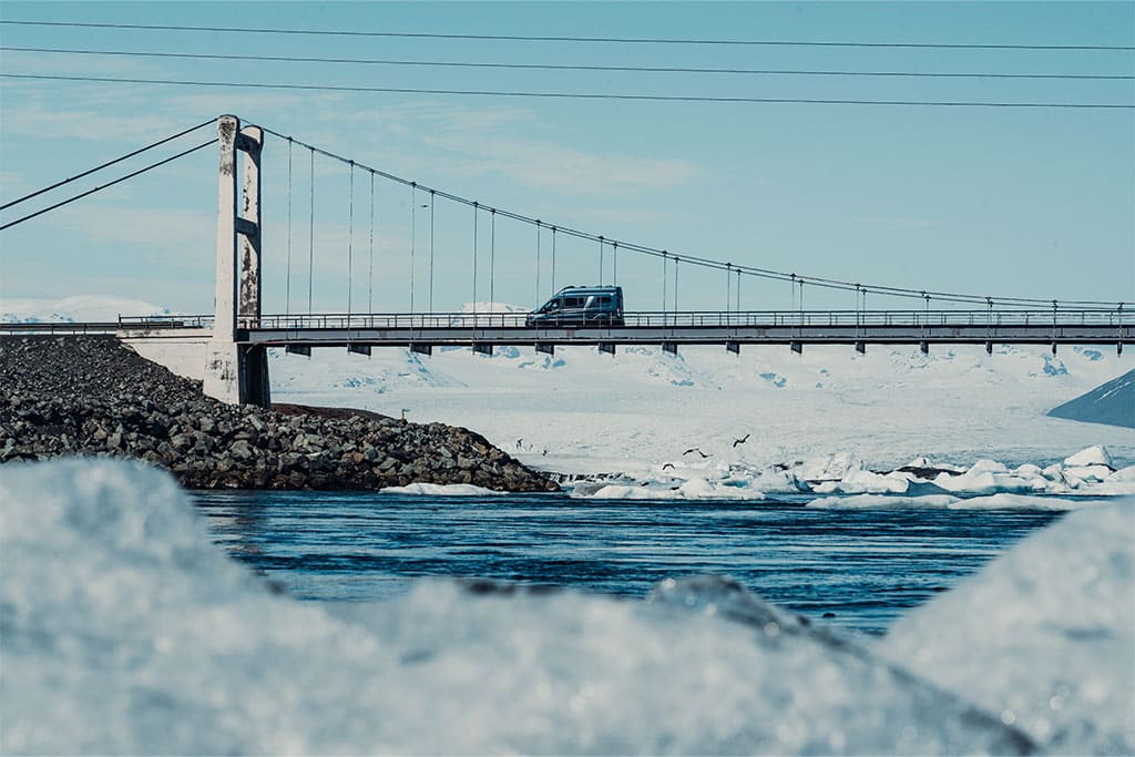 Eine Brücke führt über die Mündung der Gletscherlagune Jökulsárlón in Island, dahinter türmt sich die weiße Masse des größten Gletschers Europas auf.