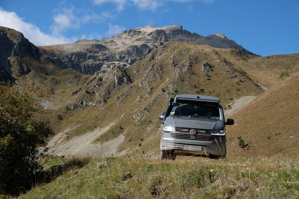 Grauer VW-Bus auf einer Offroad-Piste in bergiger Landschaft