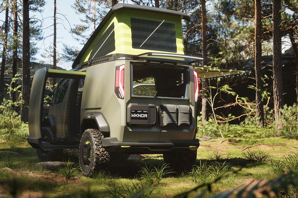 Kia PV5 WKNDR Concept Camper: Olivgrüner Offroad-Minicamper mit hellgrünem Aufstelldach auf einer Wiese zwischen Bäumen