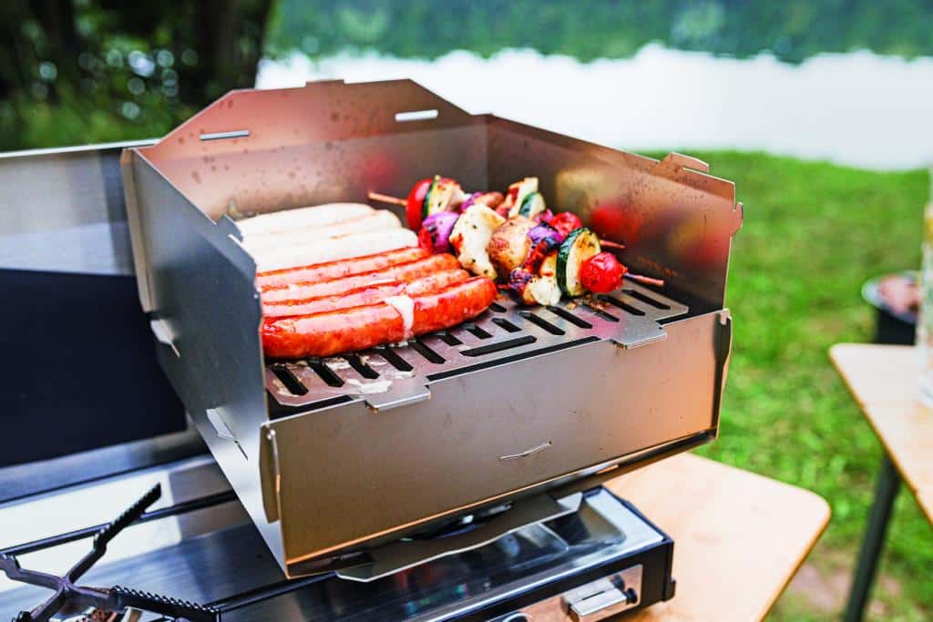 Camping-Grill mit Würstchen und Gemüsespießen