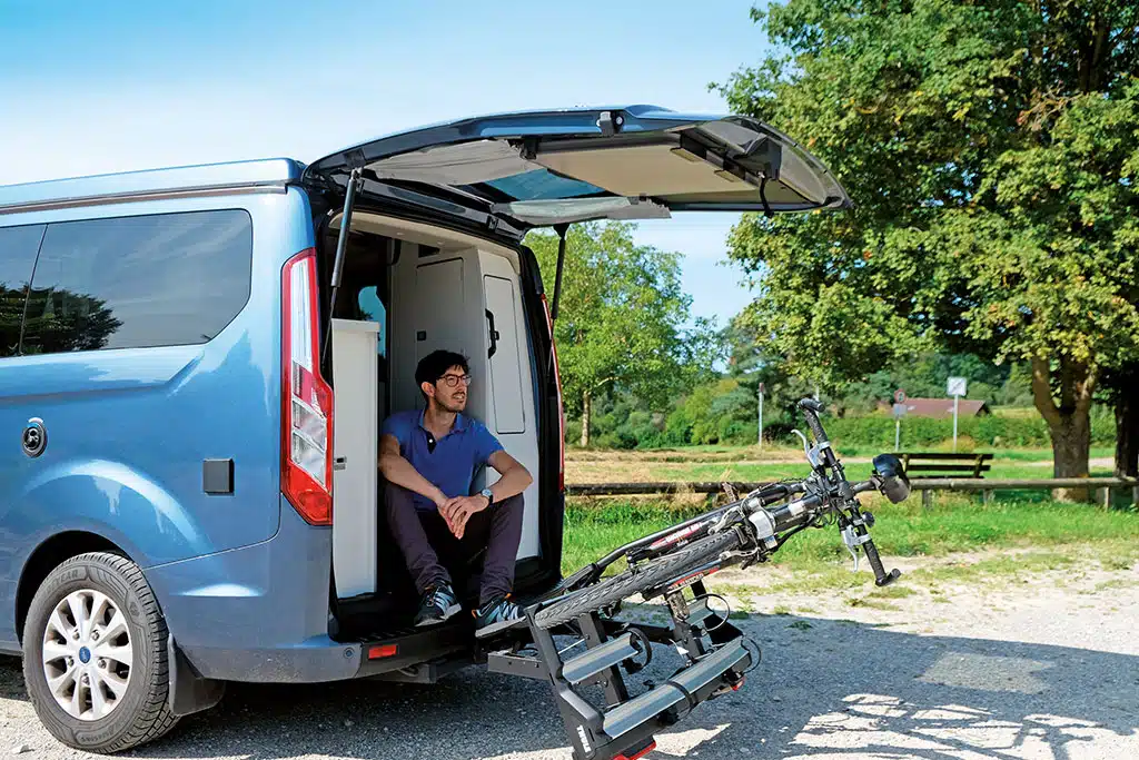 Thule Velospace XT-3 im Test: Mann sitzt im Kofferraum eines Campers, vor ihm befindet sich ein Fahrrad in einer Halterung.