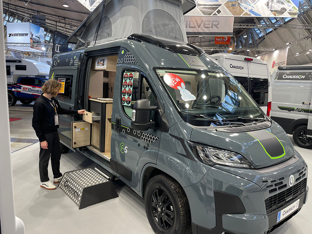 Grauer Kastenwagen mit Campingausbau und Aufstelldach in einer Messehalle