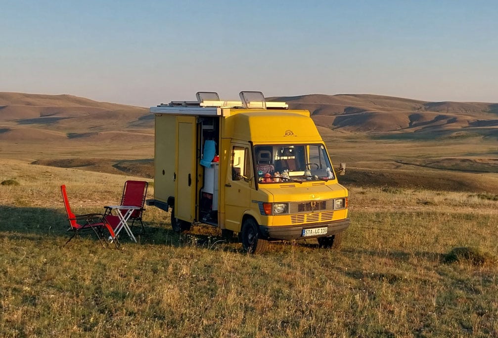 Overland Weltreise: Gelber Postbus mit Campingausbau in einer Steppenlandschaft