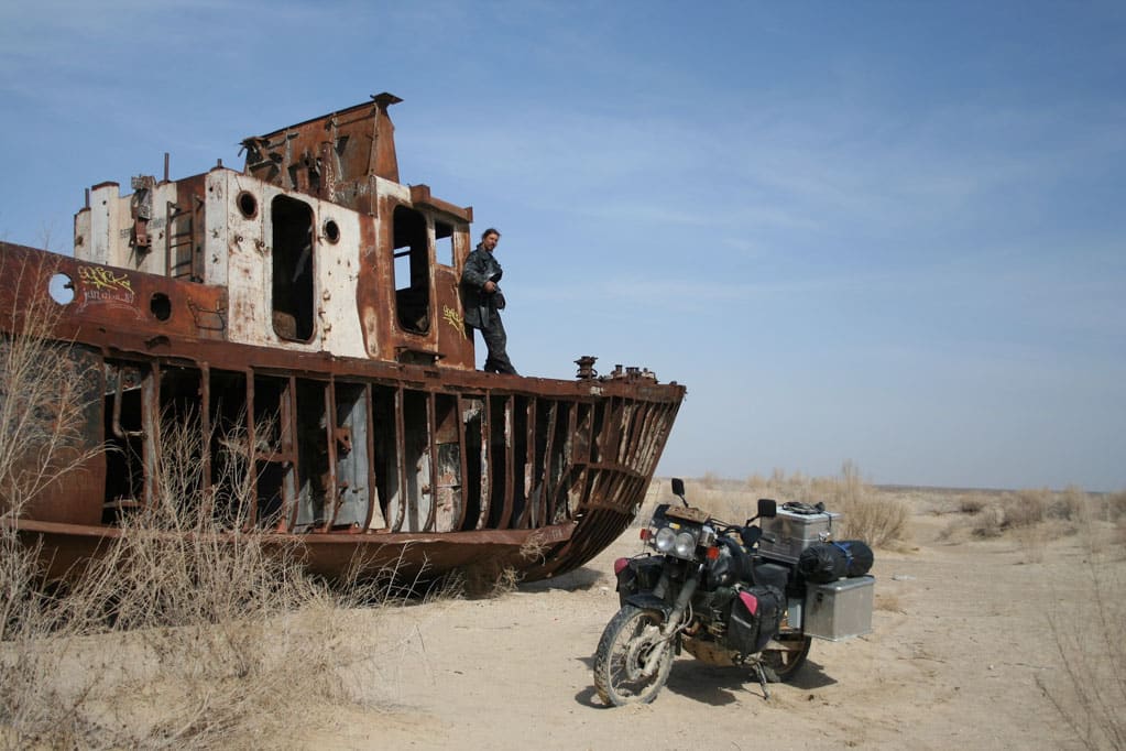 Schwarzes Motorrad vor Schiffswrack auf Sand