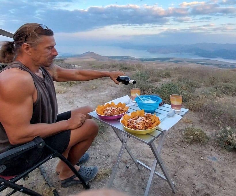 Mann am gedeckten Campingtisch in weiter, etwas karger Natur