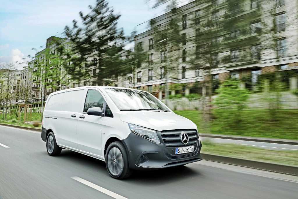 Weisser Mercedes-Benz Vito fährt vor Häuserfront mit Büschen und Bäumen